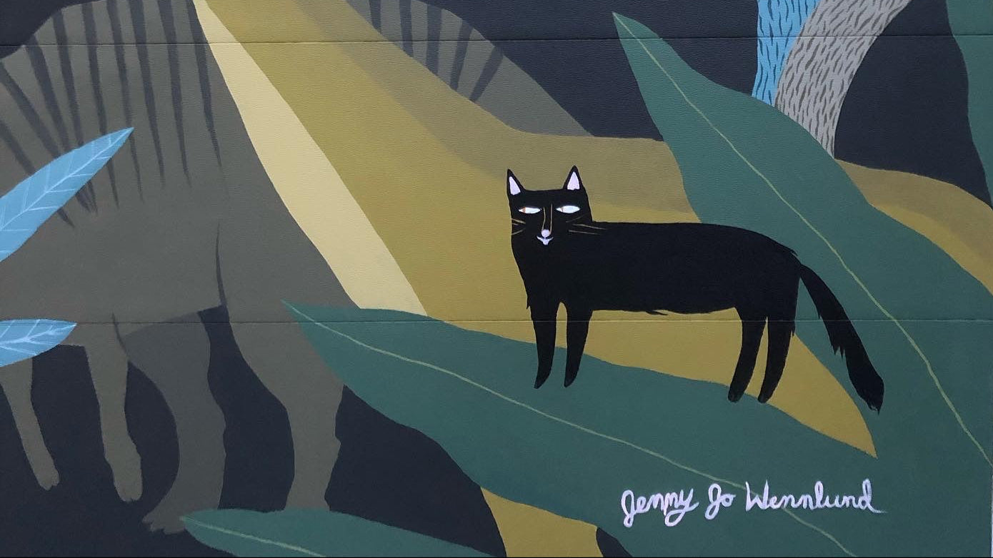 Mural of a black cat in a tropical setting with trees and plants.